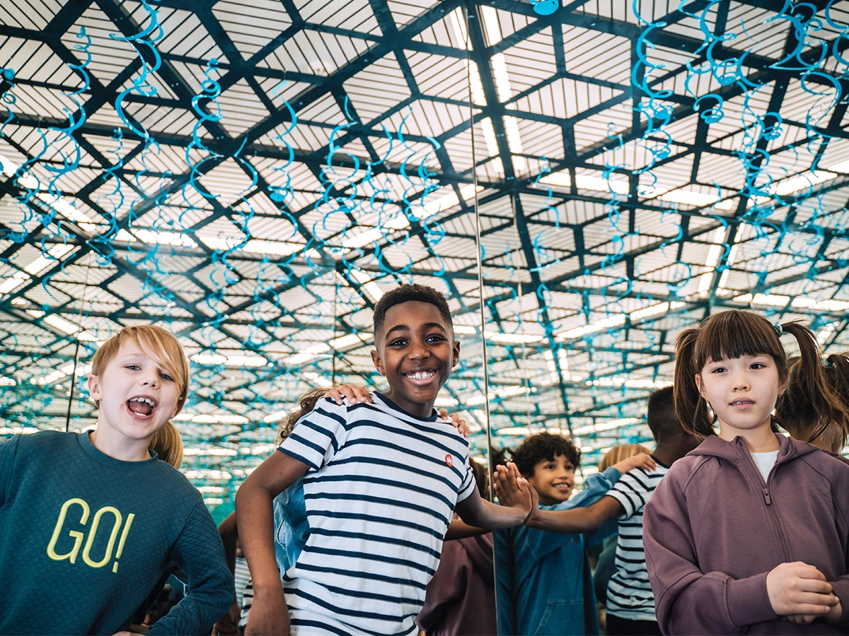 A group of children are having a fun birthday party at Museum of Illusions. They are smiling and hugging in the Infinity Room, their infinite reflections seen in the mirrors.