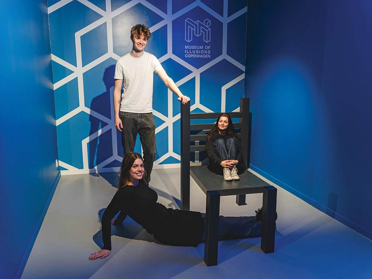 Three young people interact with the classical Beuchet Chair exhibit at an event at Museum of Illusions Copenhagen.