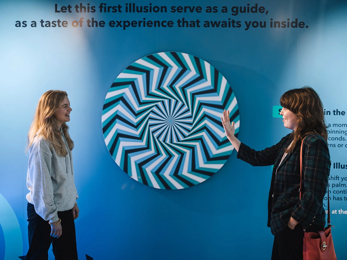 Two women in a team building are spinning an optical illusion on the wall at Museum of Illusions.