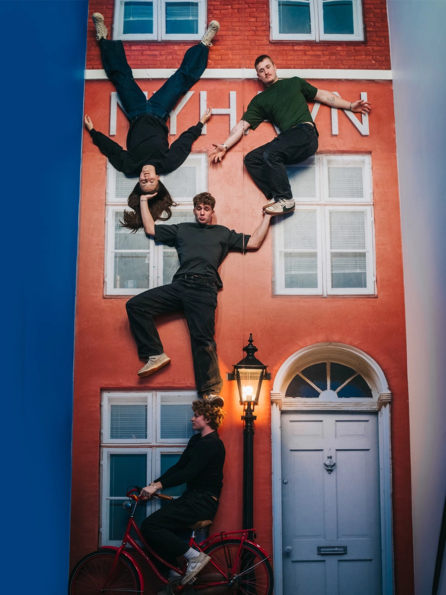 Four young persons seem to defy gravity in front of what appears to be a Nyhavn building at Museum of Illusions Copenhagen.