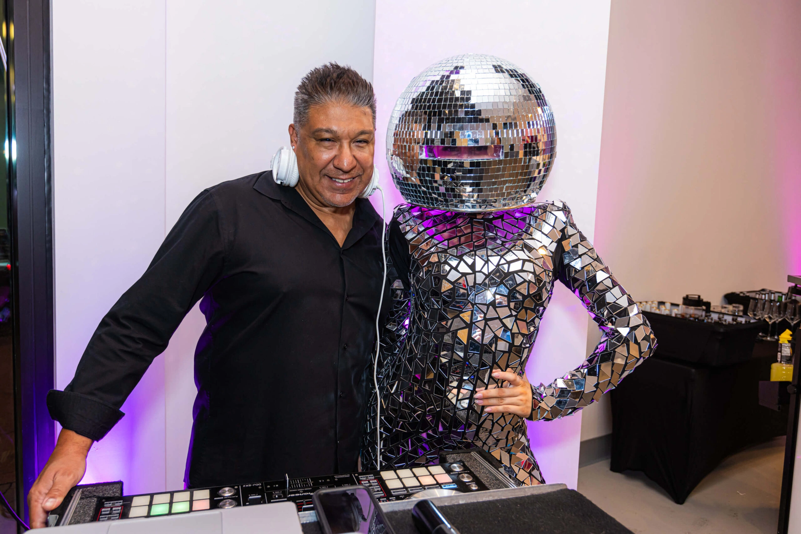A DJ is posing for a photograph with a person dressed as a disco ball at a party at Museum of Illusions.